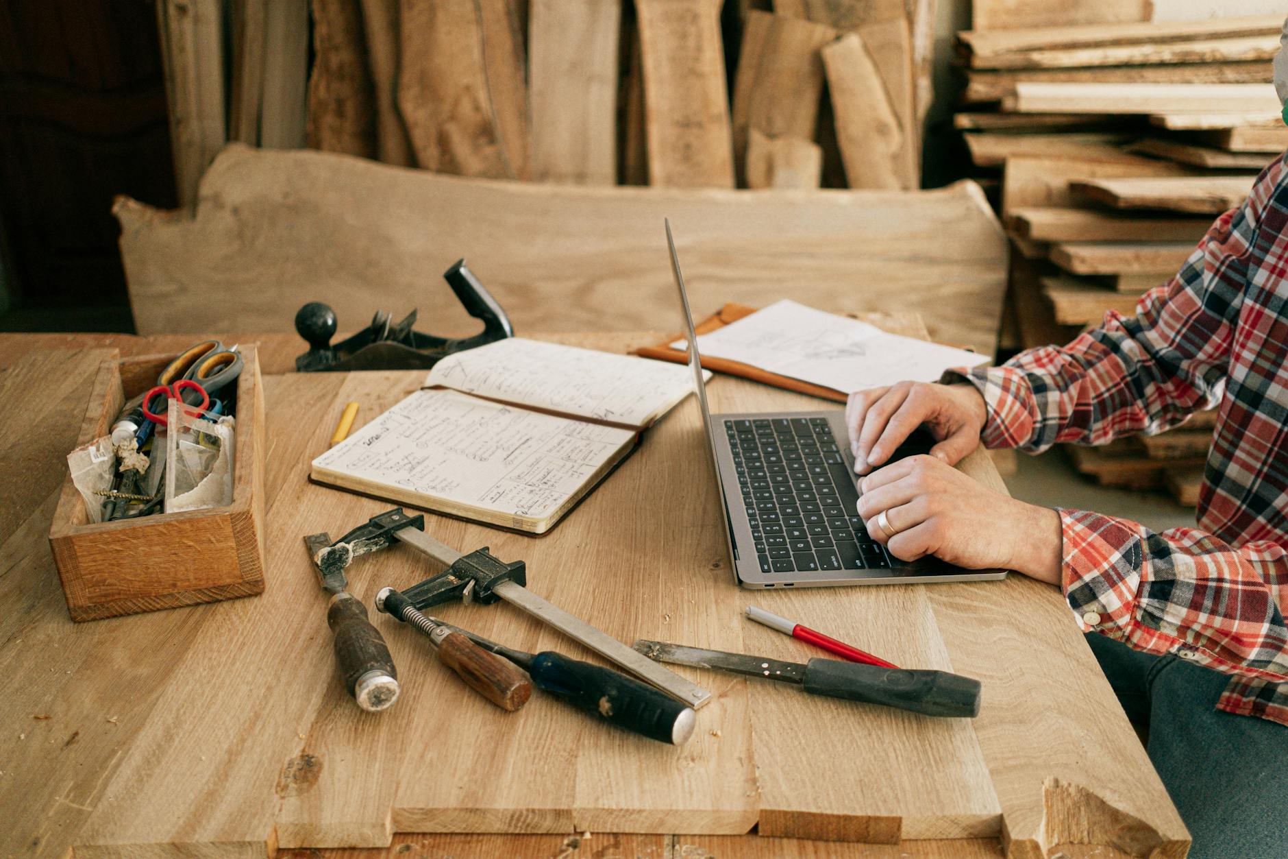 Carpenter using laptop among workshop tools symbolises blending traditional craft skills with modern web building technology 